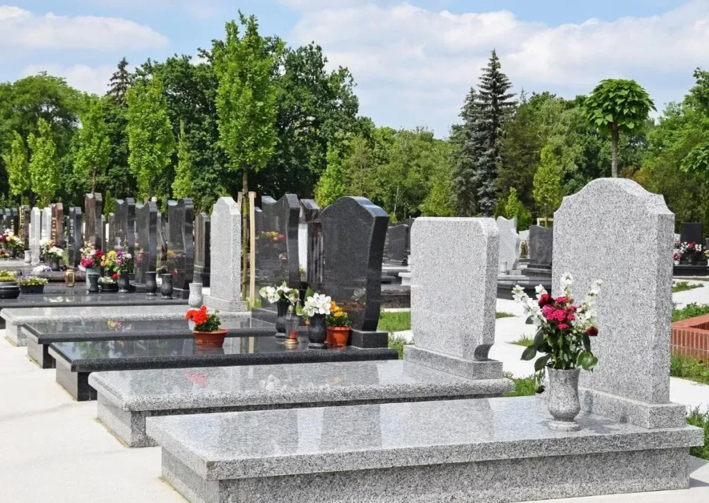 Alignement de monuments funéraires en granit gris ornés de fleurs dans un cimetière.