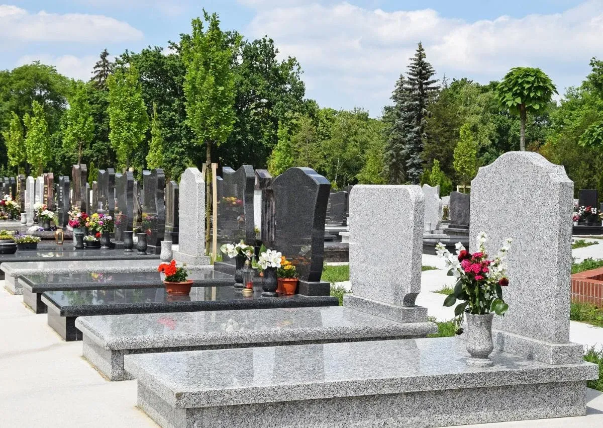 Alignement de monuments funéraires en granit gris ornés de fleurs dans un cimetière.